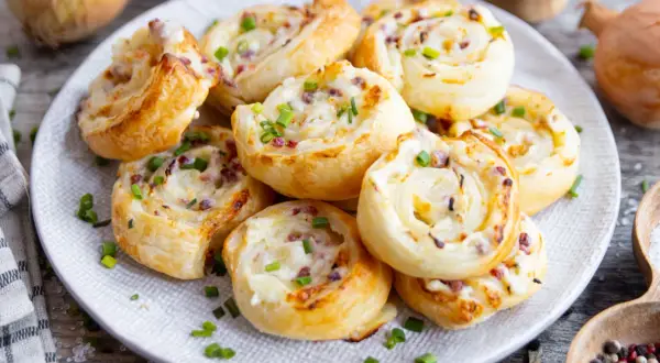 Herzhafte Flammkuchen Schnecken mit Speck und Zwiebeln, bestreut mit frischem Schnittlauch, auf einem Teller angerichtet.