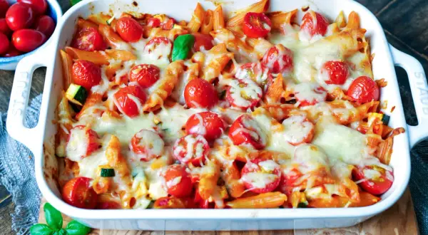 Ein köstlicher nudelauflauf vegetarisch mit Penne, Kirschtomaten und geschmolzenem Käse in einer weißen Auflaufform.