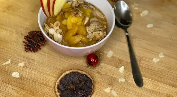 Schüssel mit Bratapfel Porridge, garniert mit Apfelscheiben und Mandelblättchen. Ein festlicher Genuss für kalte Tage.