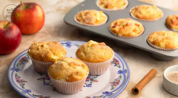 Frisch gebackene Apfelmus Muffins auf einem Teller, daneben Äpfel und Zimt.