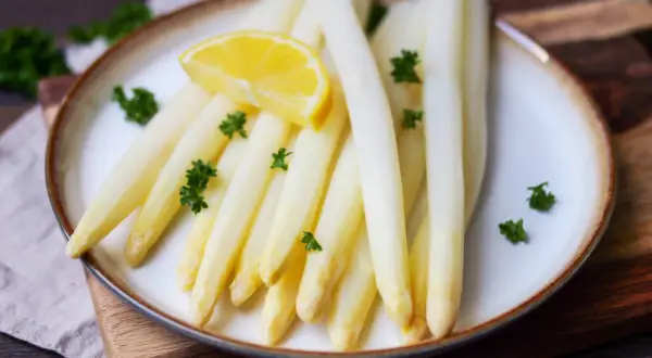 Frischer weißer Spargel, perfekt gekocht, garniert mit Petersilie und einer Zitronenspalte auf einem Teller. Ein Genuss, wenn Spargel Saison hat.