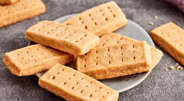 Goldbraune Shortbread-Kekse, perfekt für ein einfaches Shortbread Rezept. Sie liegen auf einem Teller und daneben ein lila Tuch.