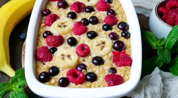 Leckere instant oats rezepte: gebackener Haferbrei mit Bananen, Himbeeren und Blaubeeren, garniert mit frischer Minze.