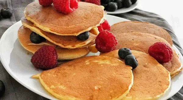 Gestapelte, goldbraune, gesunde Pancakes mit frischen Himbeeren und Blaubeeren garniert. Ein köstlicher Start in den Tag.