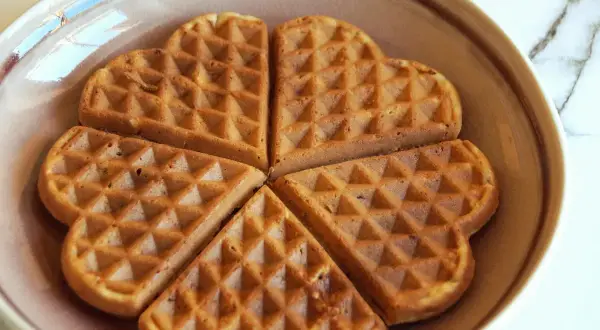 Herzförmige Waffeln ohne Zucker, goldbraun gebacken, liegen auf einem Teller.