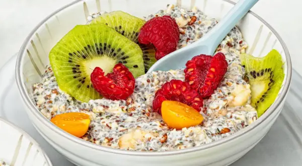 Schüssel mit Overnight Oats, garniert mit Kiwi, Himbeeren und Physalis. Ein Löffel liegt darin.
