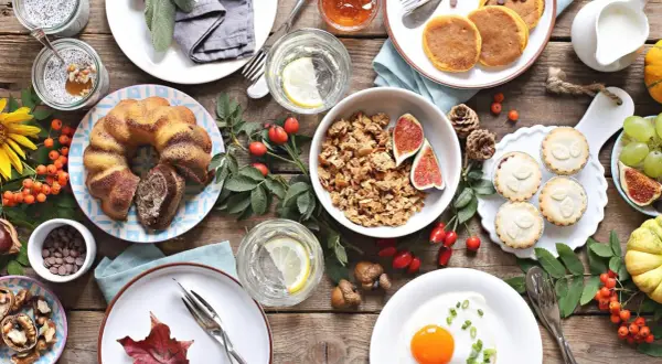Leckere Brunch-Ideen: Marmorkuchen, Pancakes, Müsli, Obst und kleine Törtchen auf rustikalem Holztisch.