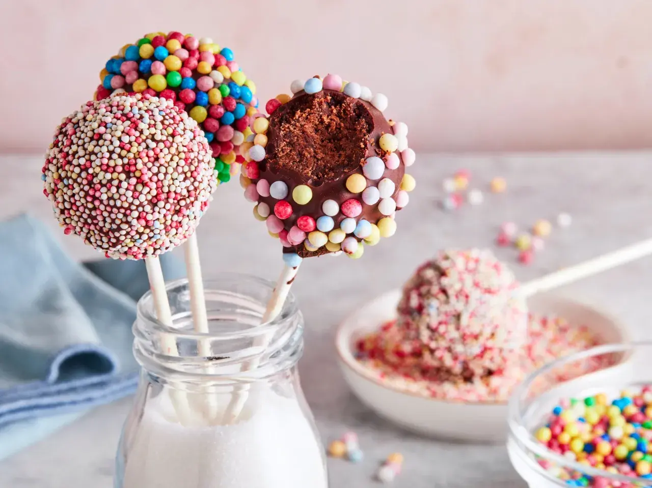 Bunte cake pops, verziert mit Zuckerstreuseln, warten darauf, vernascht zu werden. Einer ist angeknabbert und zeigt den schokoladigen Kern.