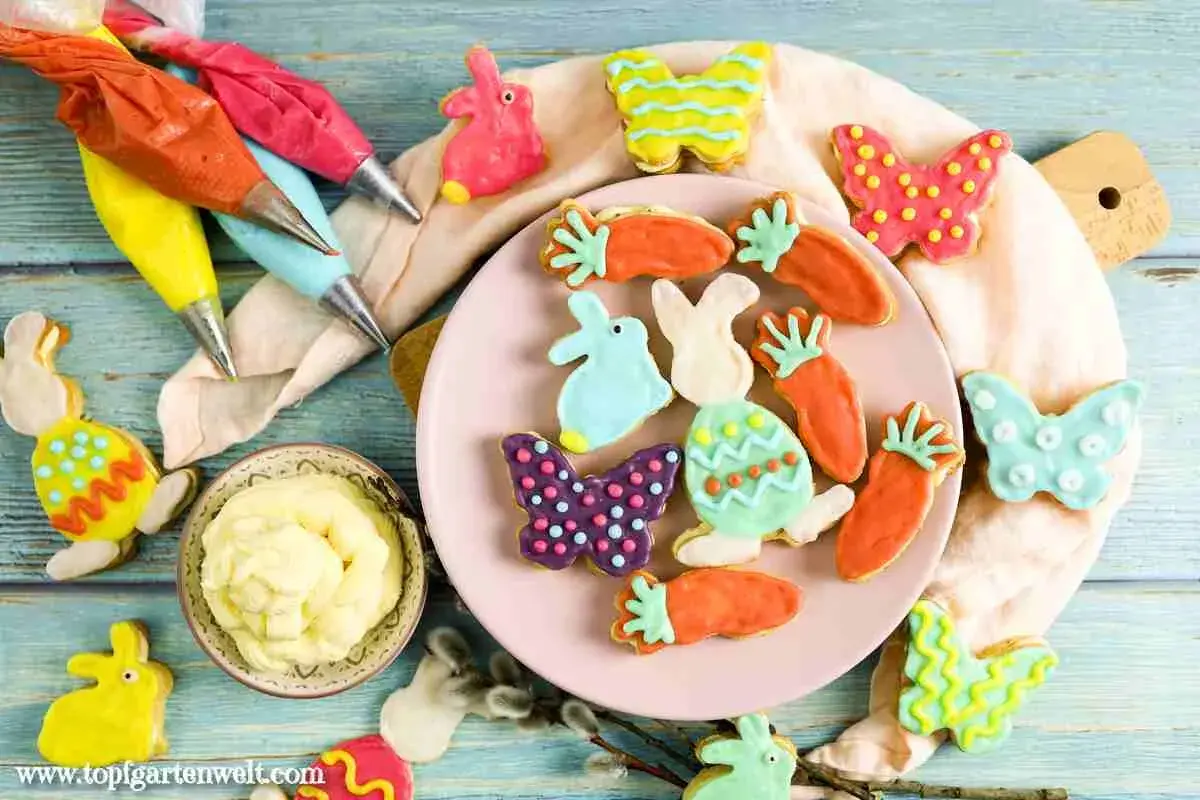 Bunte Osterkekse in Hasen-, Karotten- und Schmetterlingsformen, bereit für ein einfaches Osterkekse Rezept. Spritzbeutel mit Zuckerguss liegen bereit.