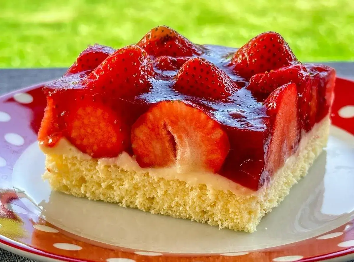 Ein Stück saftiger, **schneller Erdbeerkuchen vom Blech ohne Pudding**, belegt mit frischen Erdbeeren und glänzendem Tortenguss.