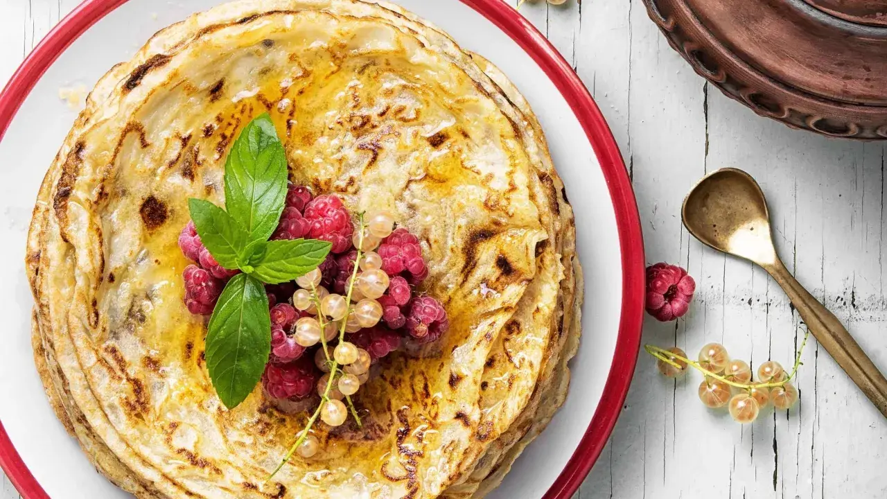 Gestapelte Pfannkuchen ohne Mehl, beträufelt mit Honig und garniert mit frischen Beeren und Minze. Ein köstlicher Genuss!