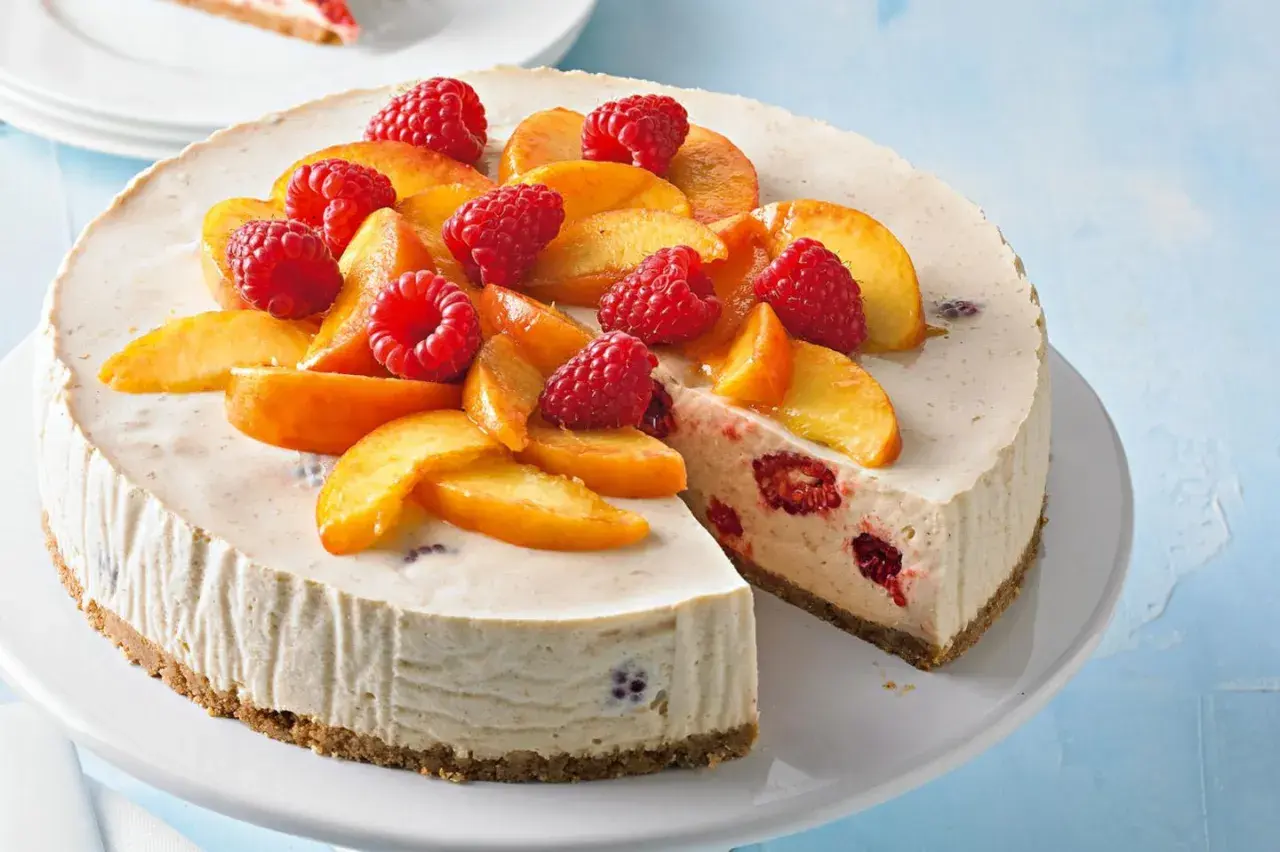 Cremiger Pfirsich Melba Kuchen mit frischen Himbeeren und Pfirsichspalten, ein Genuss für Augen und Gaumen.