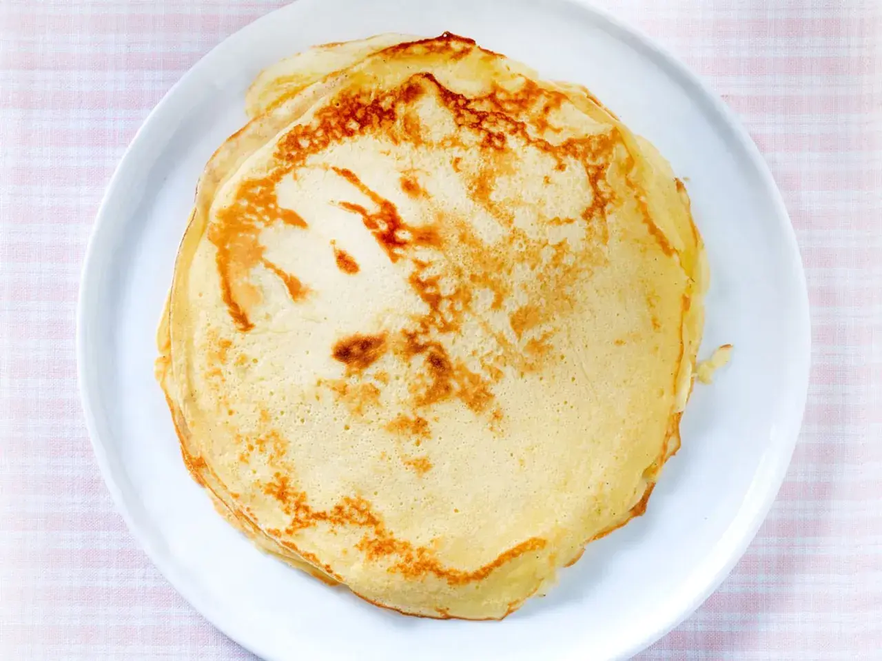 Ein Stapel goldbrauner, veganer Pfannkuchen liegt auf einem weißen Teller. Perfekt für ein leichtes Frühstück.