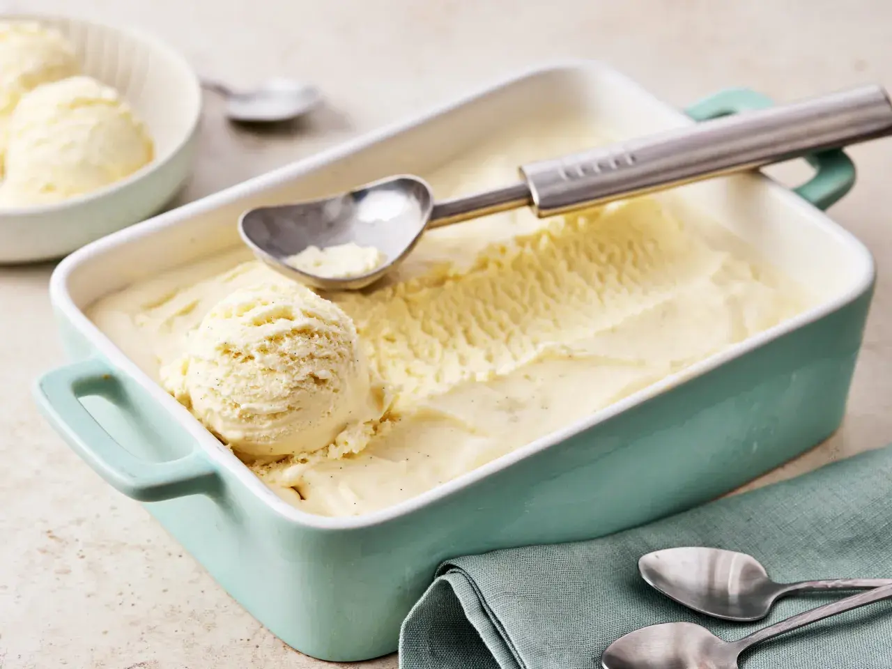 Ein Behälter mit cremigem Vanilleeis, perfekt zum vanilleeis selber machen. Ein Löffel liegt bereit, um die erste Kugel zu entnehmen.