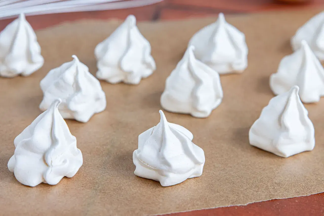 Weiße Baiser-Häufchen, bereit für das Baiser Rezept. Sie liegen auf Backpapier und sehen luftig und leicht aus.
