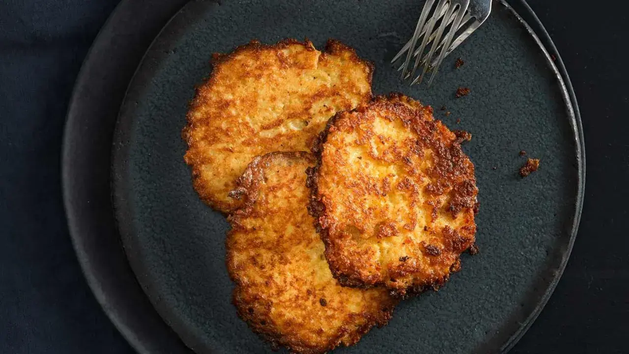 Drei goldbraune Kartoffelpuffer liegen auf einem dunklen Teller. Perfekt für den Thermomix!