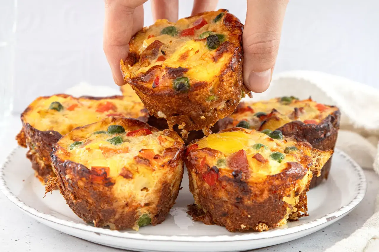 Goldbraune, herzhafte Pizza Muffins mit bunten Gemüsestückchen und Käse, die gerade aus dem Ofen kommen.