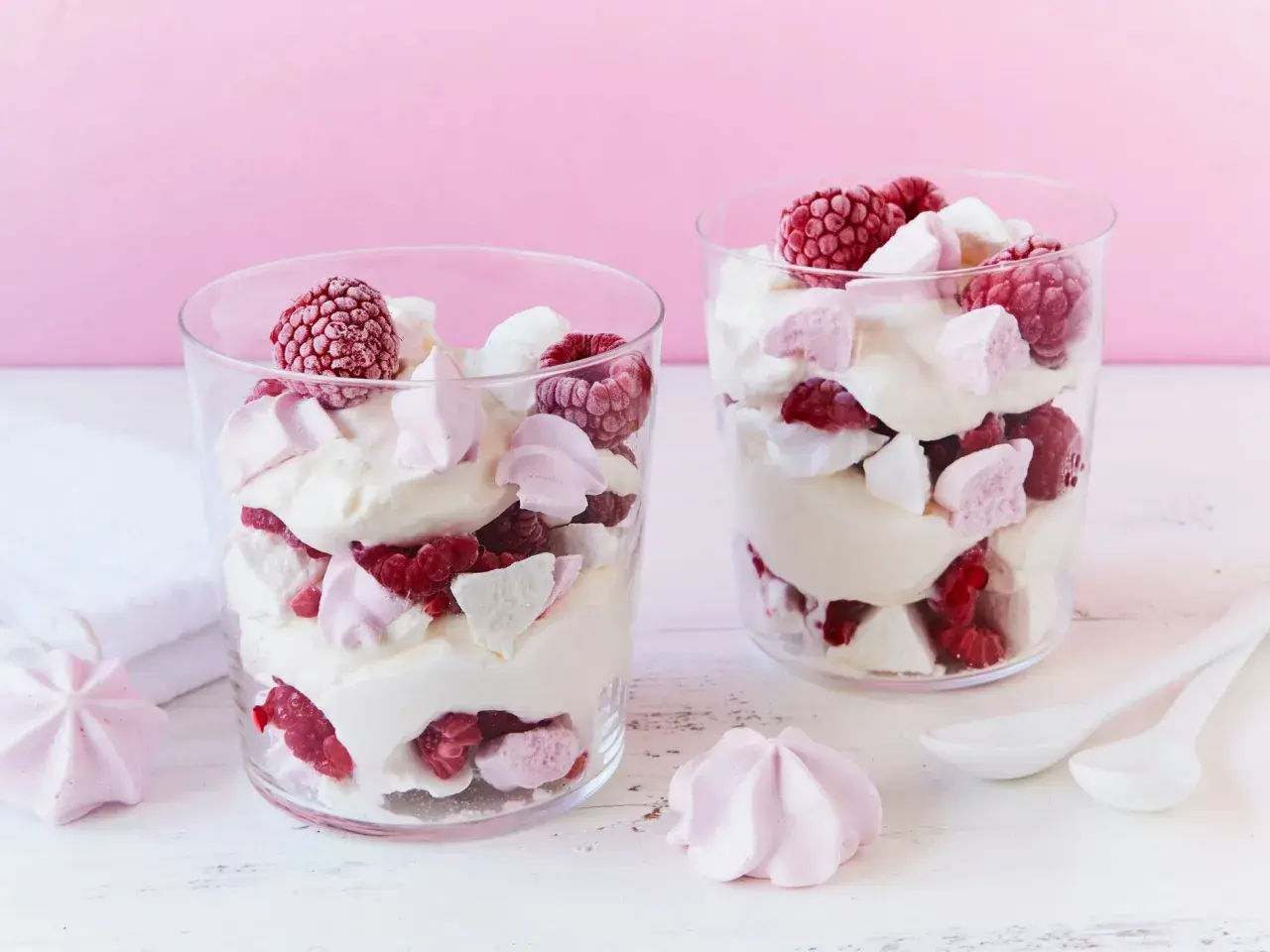 Zwei Gläser mit Himbeer Baiser Dessert, geschichtet mit Sahne, frischen Himbeeren und Baiserstückchen.