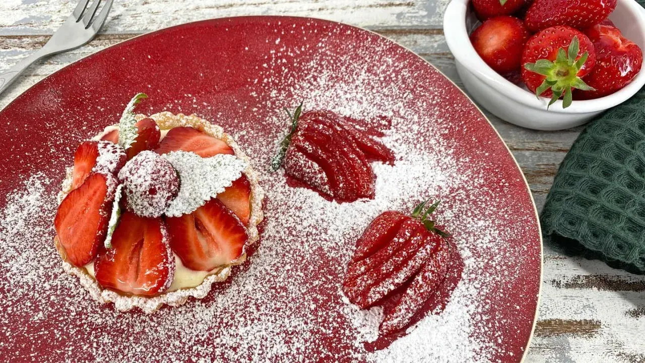 Zuckersüße Erdbeer Tartelettes, bestäubt mit Puderzucker, auf rotem Teller. Daneben frische Erdbeeren und eine kleine Schale voller roter Früchte.