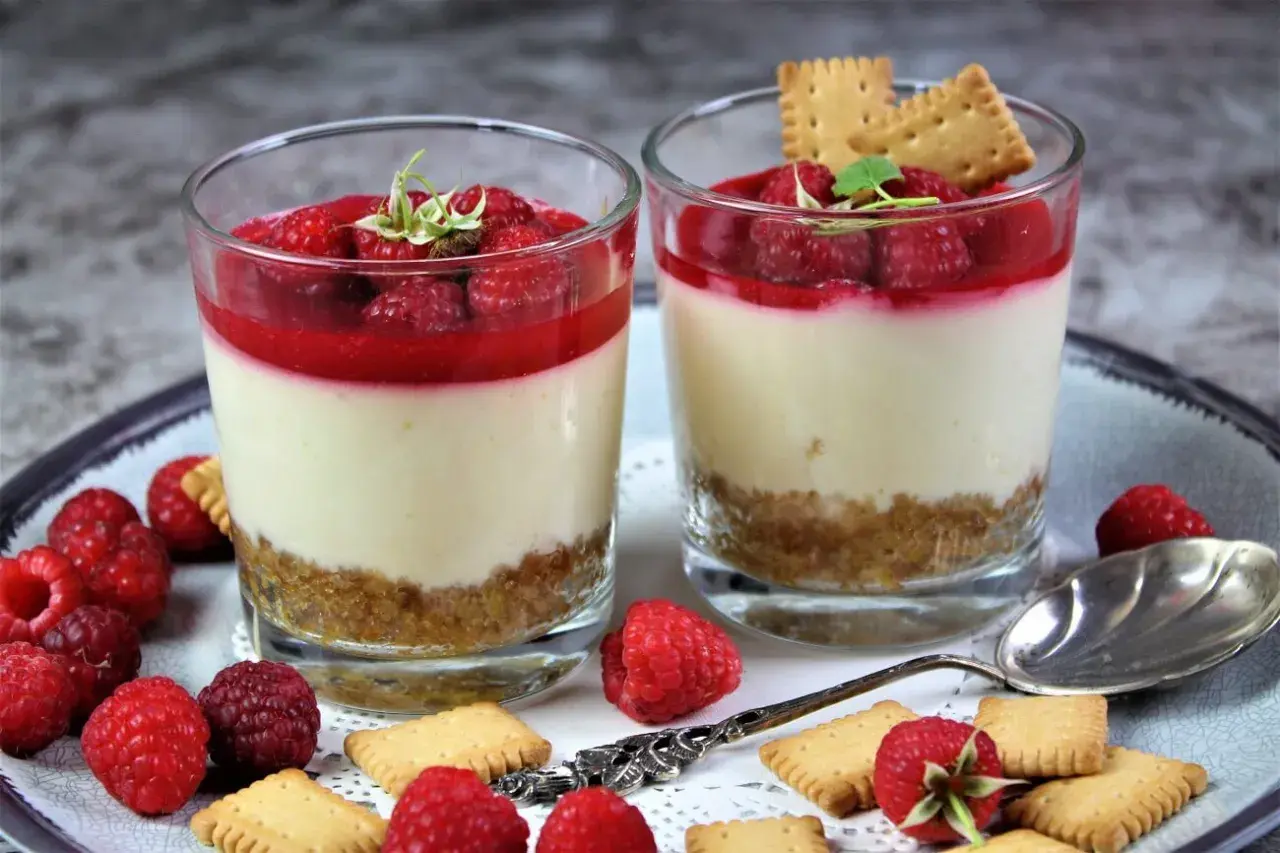 Zwei Gläser mit cremigen Desserts, garniert mit Himbeeren und Keksen. Perfekt für Ihre nächsten Dessert Rezepte.