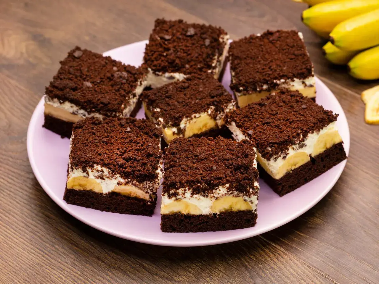 Saftiger Maulwurfkuchen vom Blech mit Bananen und Schokostreuseln auf einem rosa Teller.