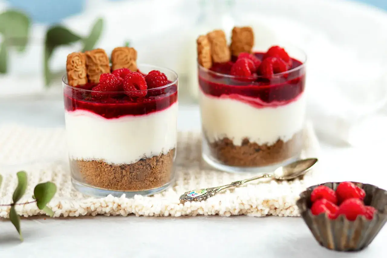 Zwei Gläser mit einem köstlichen, warmer nachtisch: Kekskrümel, cremige Schicht, Himbeersoße und frische Beeren.