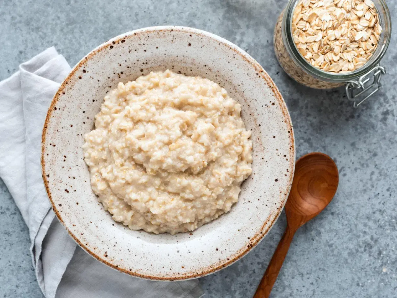 Cremiger Haferbrei in einer Schale, daneben ein Glas Haferflocken. Ein einfaches Porridge Rezept für einen gesunden Start.