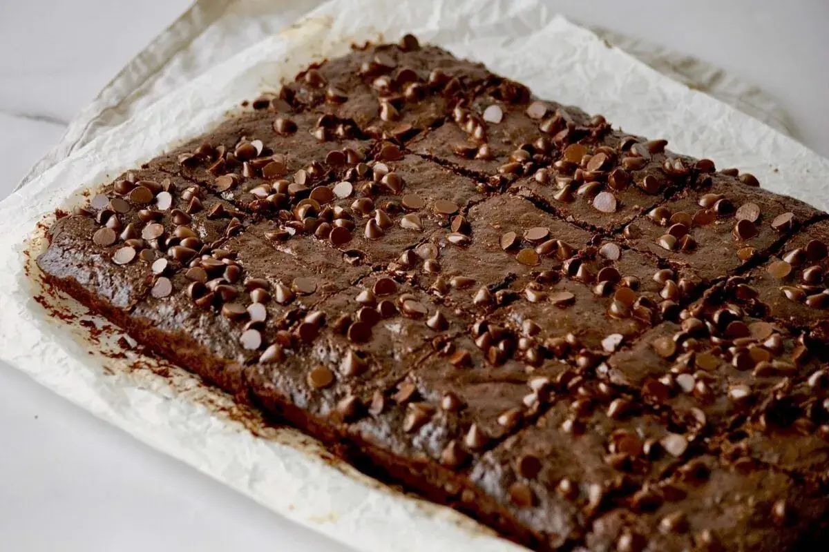 Saftige Zucchini-Brownies, bestreut mit Schokoladenstückchen, auf Backpapier.