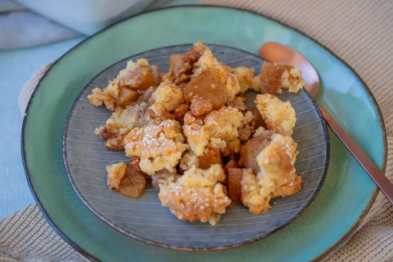 Ein Teller mit köstlichem Apfel-Crumble, bestäubt mit Puderzucker. Die warmen Apfelstücke und die knusprige Streuselhaube laden zum Genießen ein.