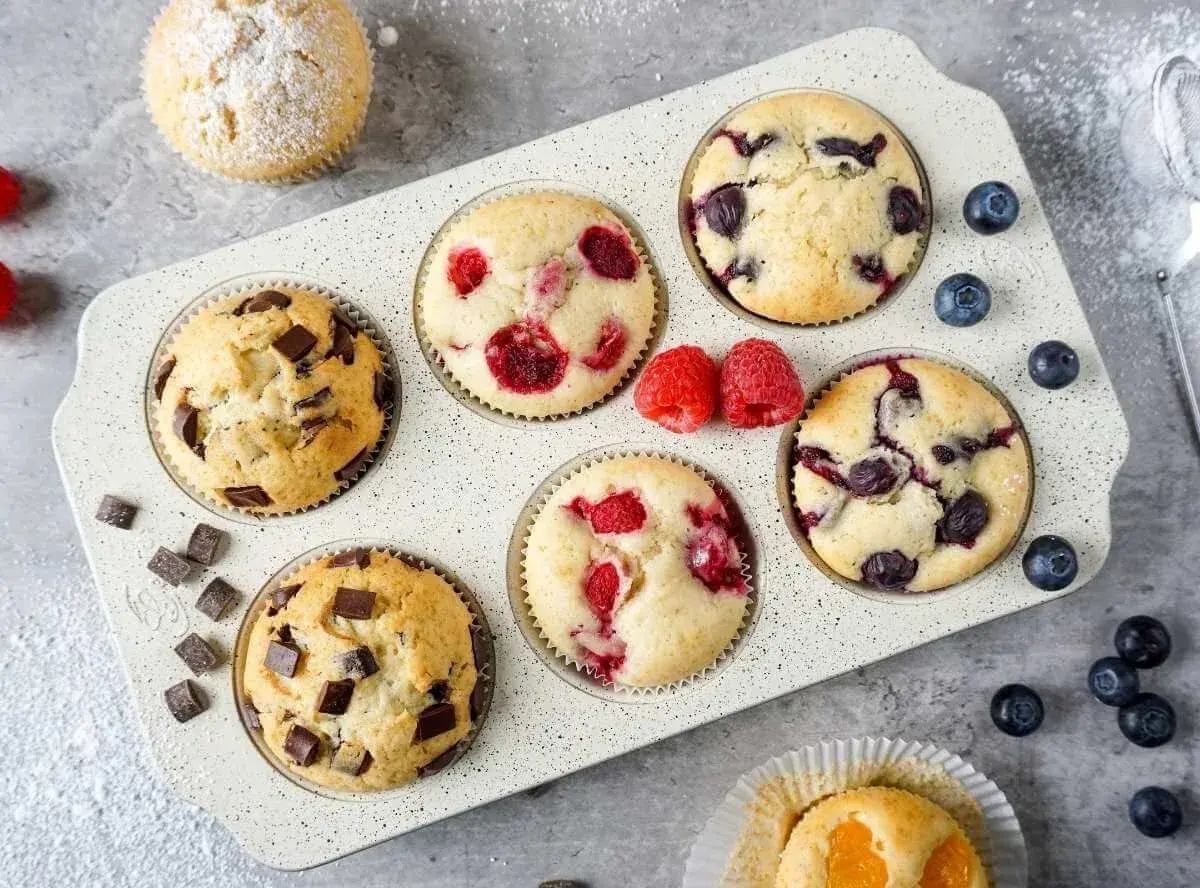 Leckeres mini muffins rezept: Schoko-, Himbeer- und Blaubeermuffins in einer Muffinform, garniert mit frischen Beeren und Puderzucker.