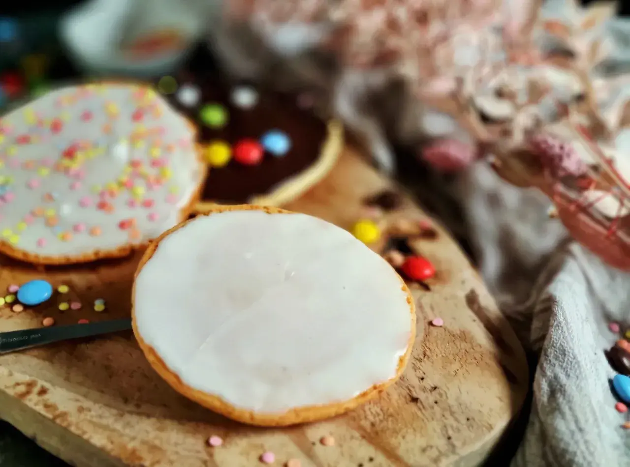 Bunte Kekse mit Zuckerguss und Schokoladenglasur, inspiriert von einem amerikanischen Rezept, liegen auf einem Holzbrett.