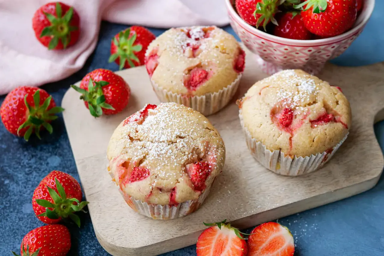 Saftige Erdbeermuffins, perfekt für jeden Kindergeburtstag, mit Puderzucker bestäubt und frischen Erdbeeren garniert.