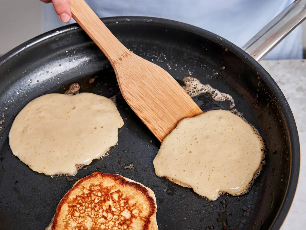 Buttermilch pancakes bräunen in der Pfanne, eine Holzspachtel wendet sie.