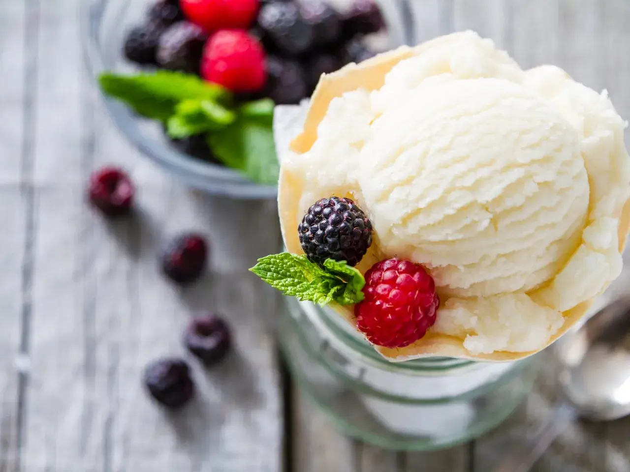 Cremiges Joghurteis selber machen: Eine Portion mit frischen Beeren und Minze garniert, daneben eine Schüssel voller Beeren.