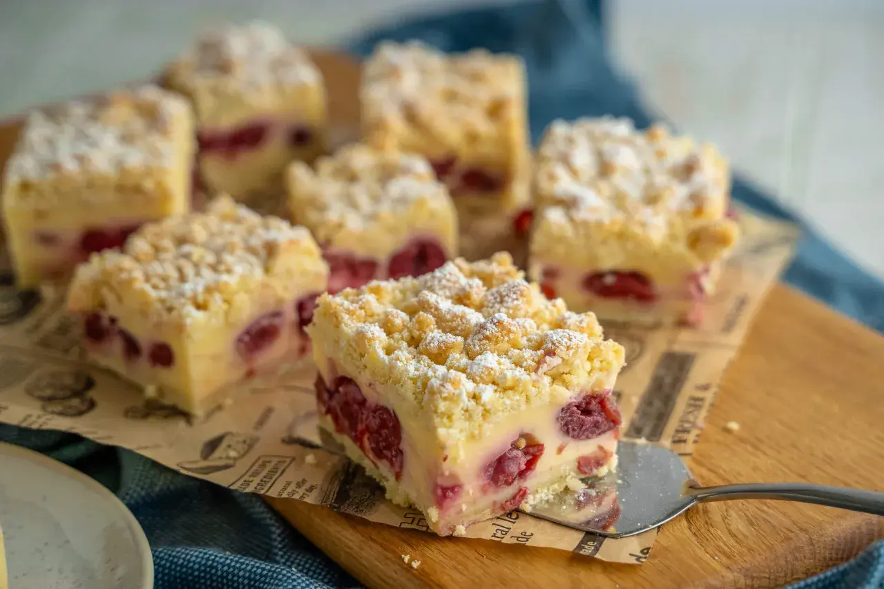 Saftiger Kirschkuchen mit Pudding und Streuseln, bestäubt mit Puderzucker. Ein Stück wird gerade serviert.