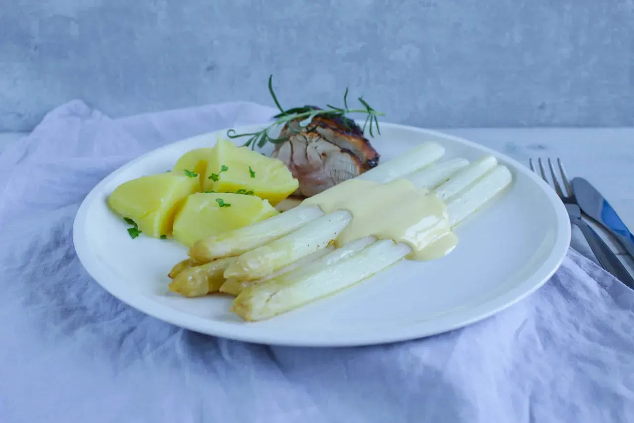 Weißer Spargel mit Sauce Hollandaise, Kartoffeln und Fleisch auf einem Teller.