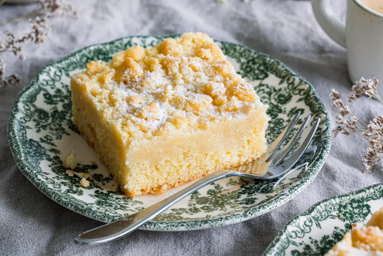 Ein Stück Streuselkuchen ohne Hefe, bestäubt mit Puderzucker, auf einem Teller mit grünem Muster.