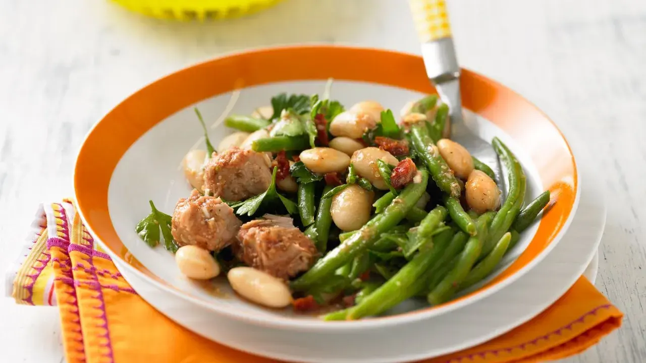Bohnensalat rezept: Frischer Bohnensalat mit weißen Bohnen, grünen Bohnen, Thunfisch und Kräutern auf einem Teller mit orangem Rand.