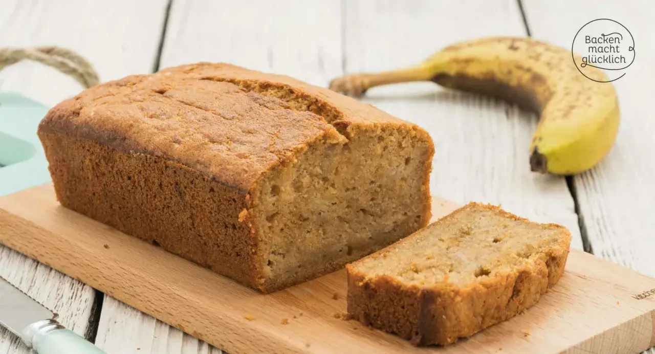 Saftiges Bananenbrot mit Dinkelmehl, frisch gebacken und auf einem Holzbrett angerichtet. Eine Scheibe ist bereits abgeschnitten.