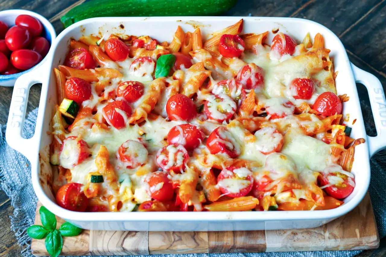 Ein köstlicher nudelauflauf vegetarisch mit Penne, Kirschtomaten und geschmolzenem Käse in einer weißen Auflaufform.