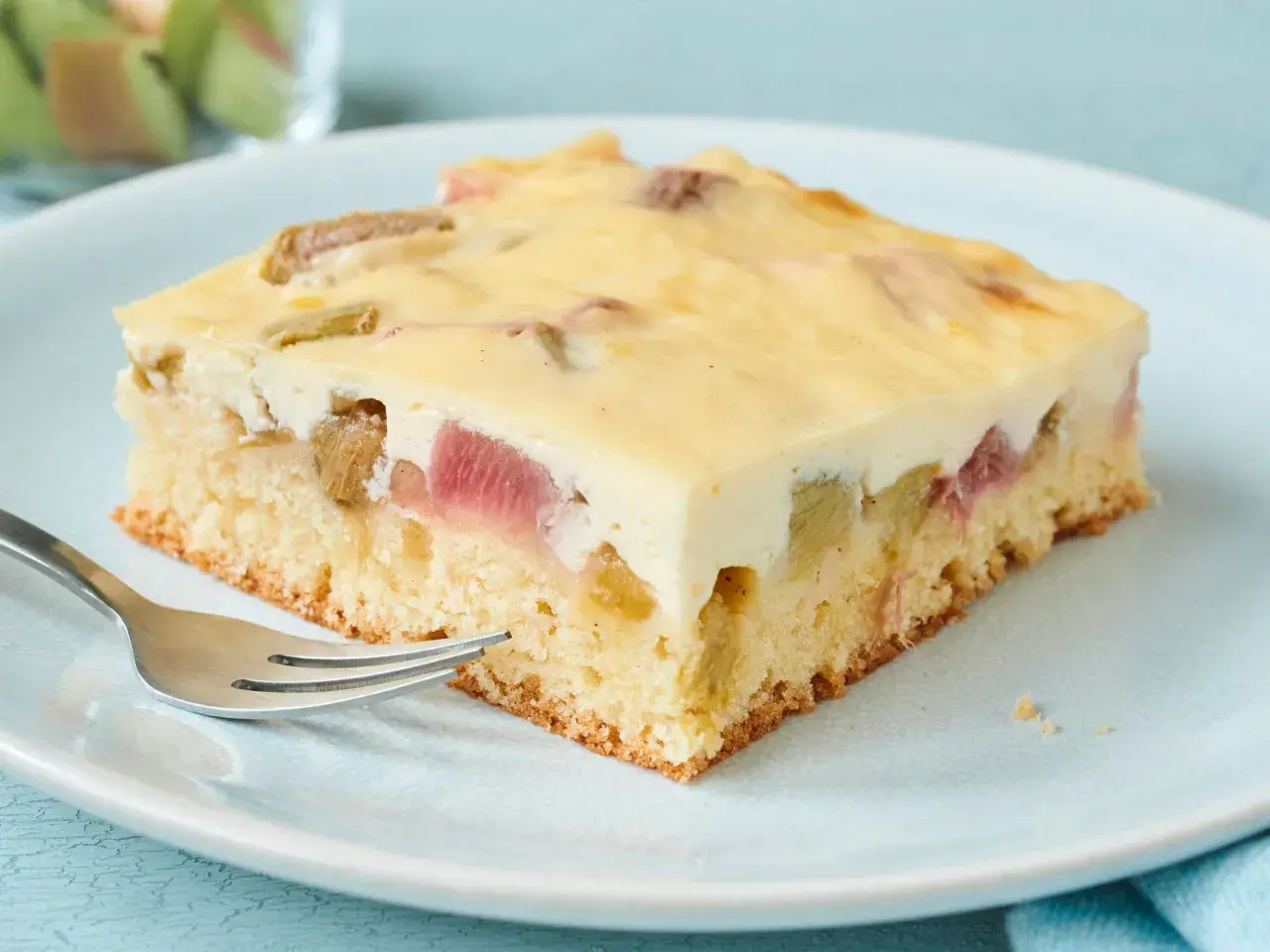 Ein Stück saftiger Rhabarber-Blechkuchen mit cremiger Füllung und einem lockeren Boden, bereit zum Genießen.