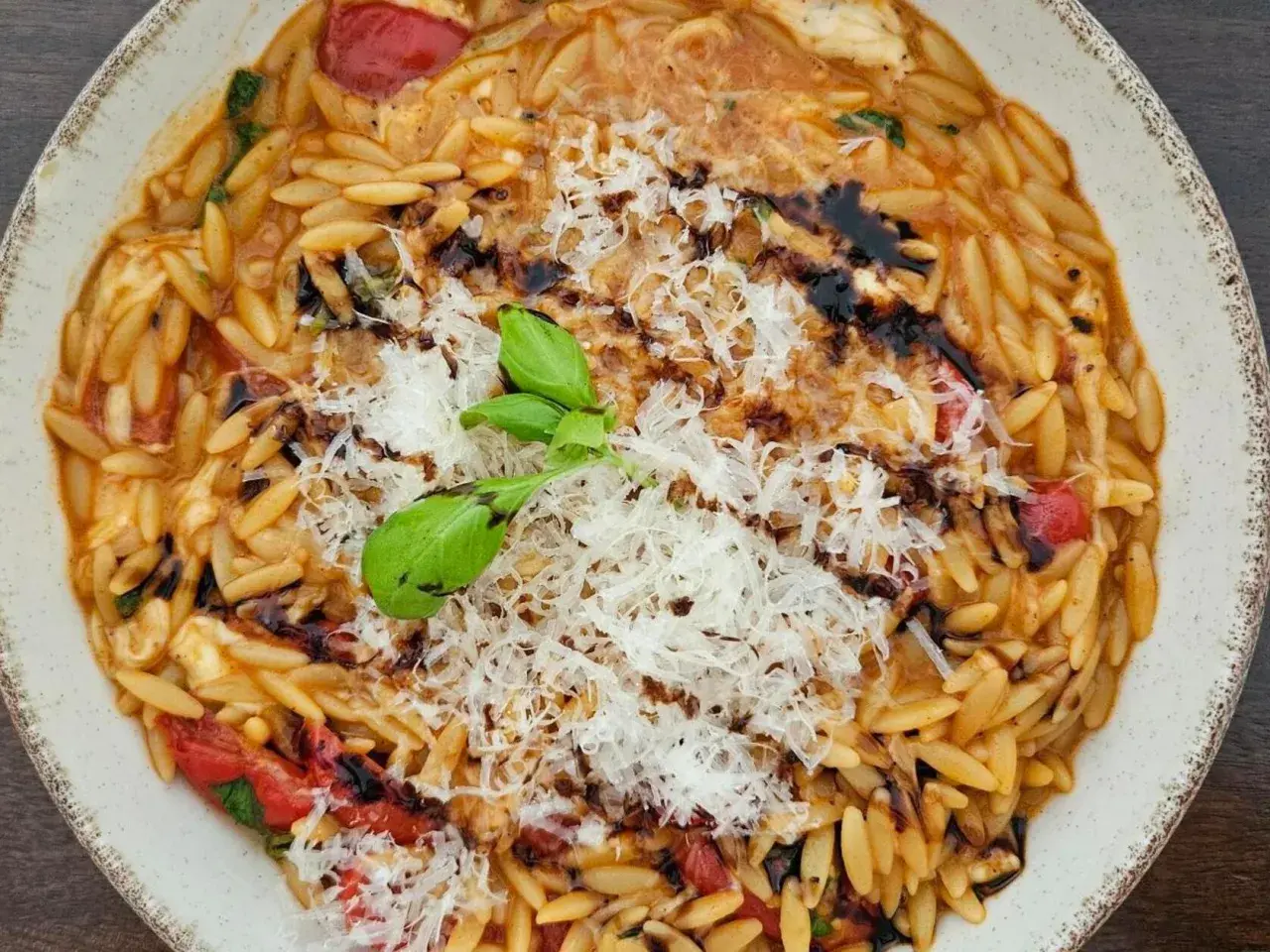 Ein Teller mit cremigen Orzo Nudeln, garniert mit geriebenem Parmesan, frischem Basilikum und Balsamico-Glasur.