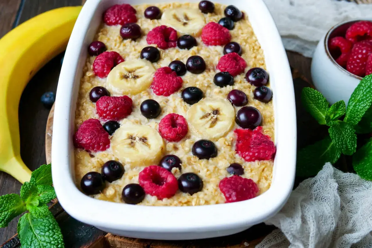 Leckere instant oats rezepte: gebackener Haferbrei mit Bananen, Himbeeren und Blaubeeren, garniert mit frischer Minze.