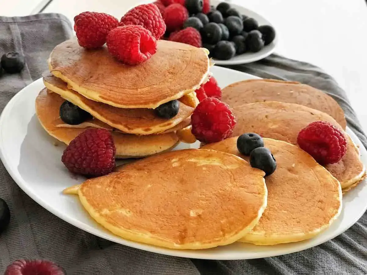 Gestapelte, goldbraune, gesunde Pancakes mit frischen Himbeeren und Blaubeeren garniert. Ein köstlicher Start in den Tag.