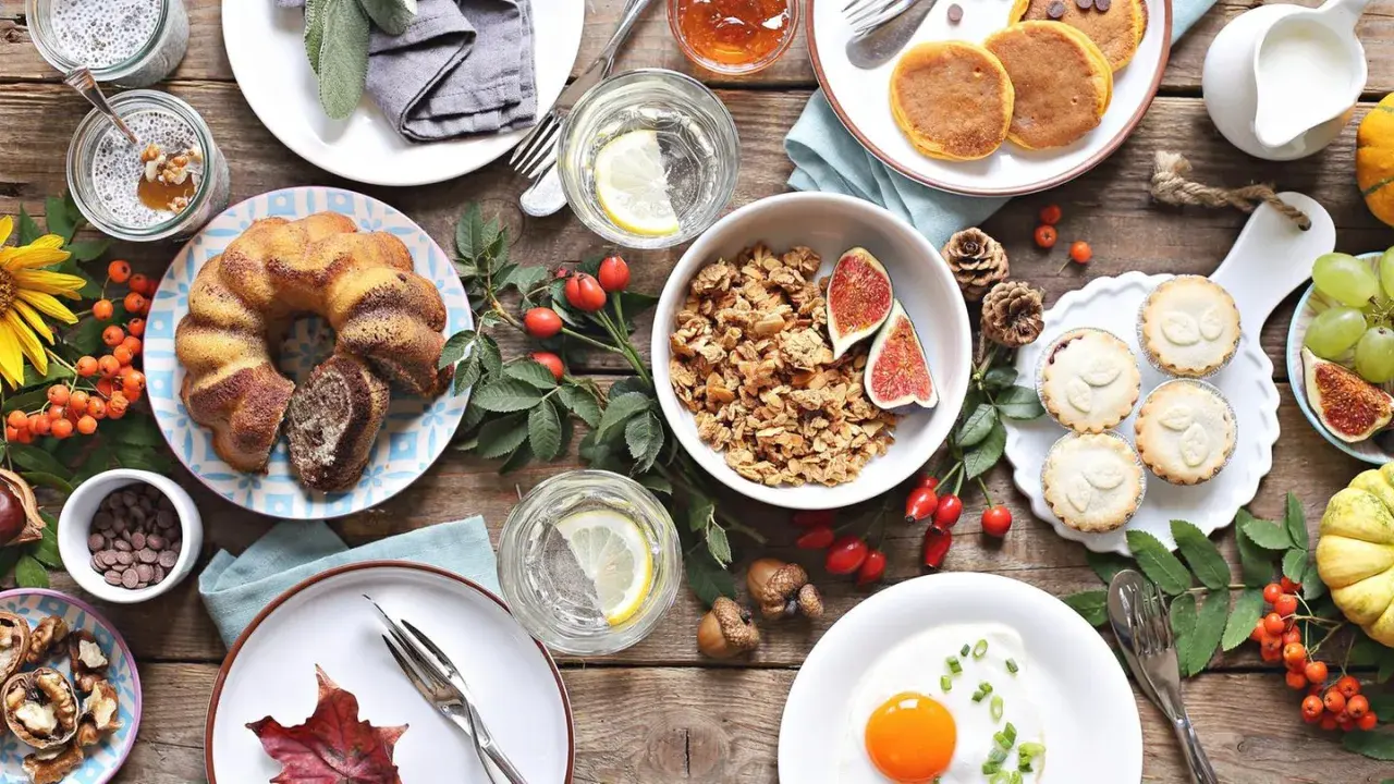 Leckere Brunch-Ideen: Marmorkuchen, Pancakes, Müsli, Obst und kleine Törtchen auf rustikalem Holztisch.