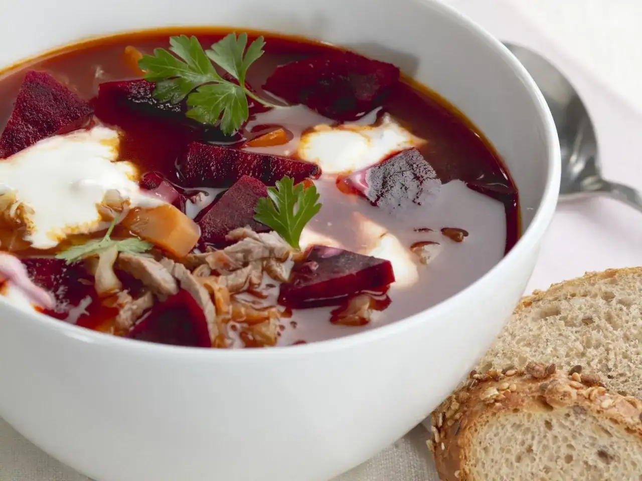 Herzhaftes Borschtsch-Rezept: Rote Bete, Fleisch und ein Klecks Sahne in einer Schüssel, dazu Brot.
