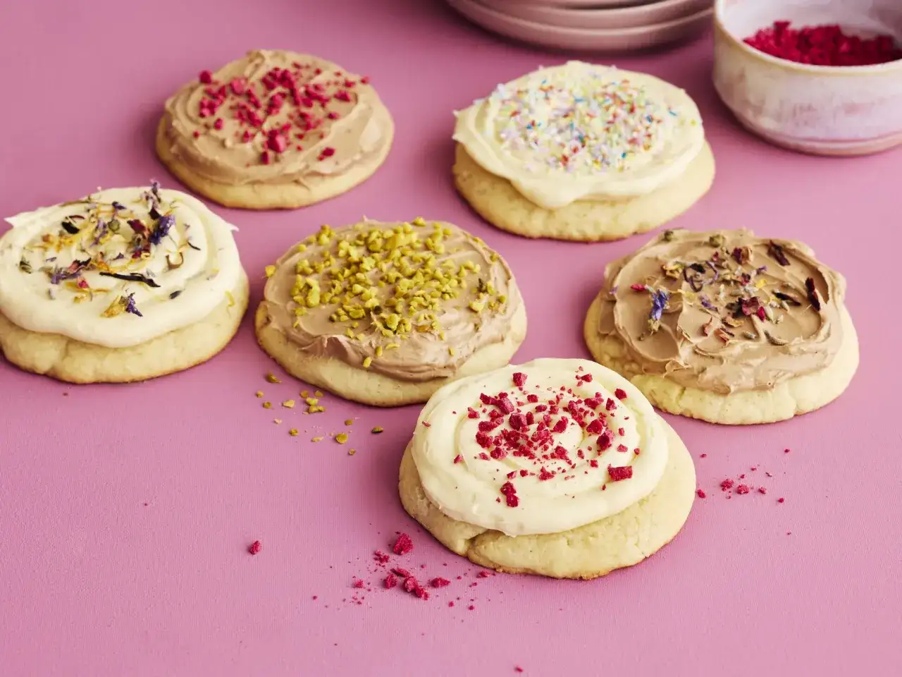 Sechs bunte Crumble Cookies mit verschiedenen Toppings: Himbeeren, Pistazien, essbare Blüten und Streusel.