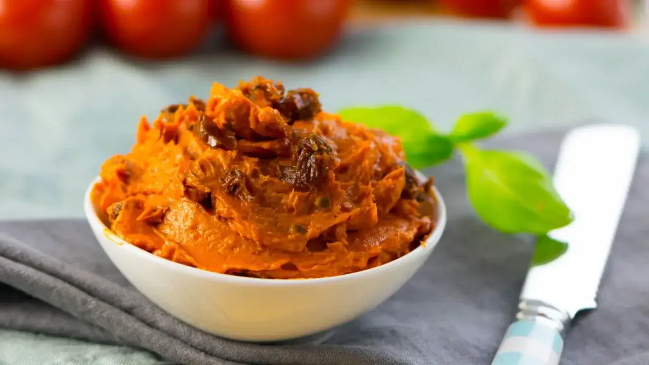 Cremige italienische Tomatenbutter mit getrockneten Tomatenst&uuml;ckchen in einer Schale, garniert mit Basilikum.