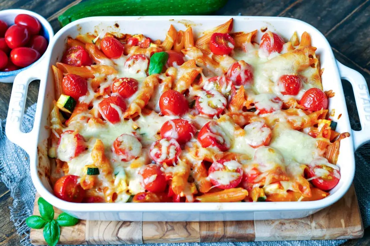 Ein köstlicher nudelauflauf vegetarisch mit Penne, Kirschtomaten und geschmolzenem Käse, garniert mit frischem Basilikum.