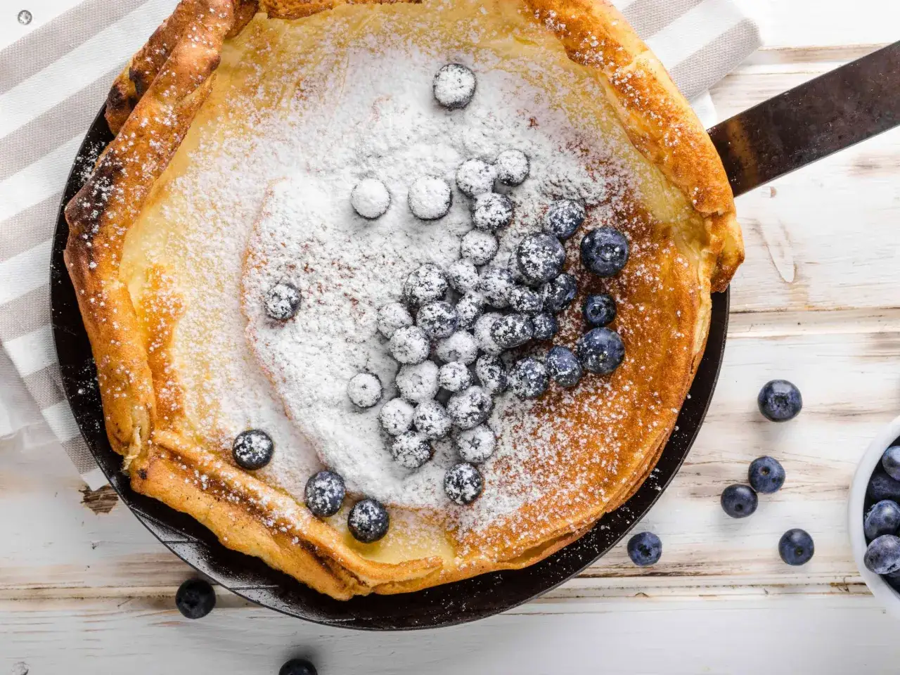 Ein goldbrauner Dutch Baby mit Puderzucker und Blaubeeren, bereit zum Genie&szlig;en.